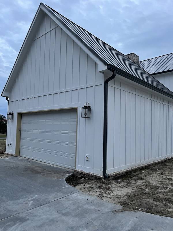 Black gutter and downspout on a white board-and-batten garage with a dark metal roof