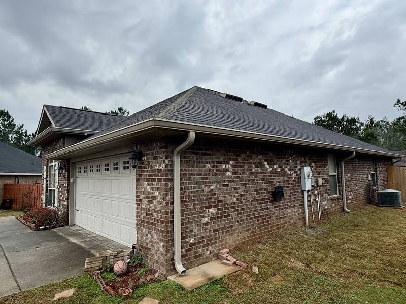 Brick ranch home with light gutters and a downspout at the garage corner