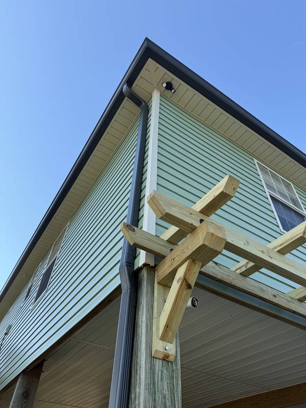 Dark bronze gutter and downspout on a green-sided house beside a new pergola