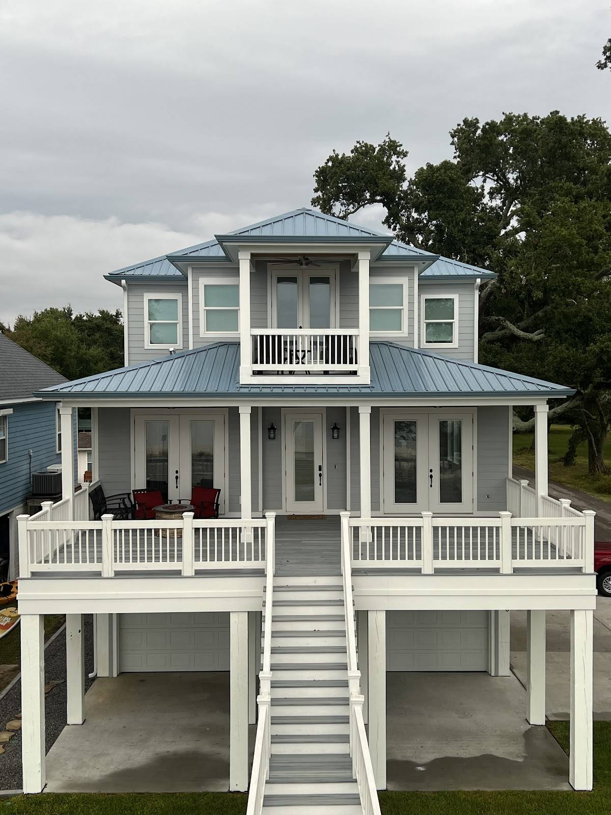 Raised two-story coastal home with a blue metal roof and white porches